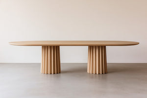 Oval dining table in light natural oak with two fluted pedestal bases, showcasing modern and minimalist design.